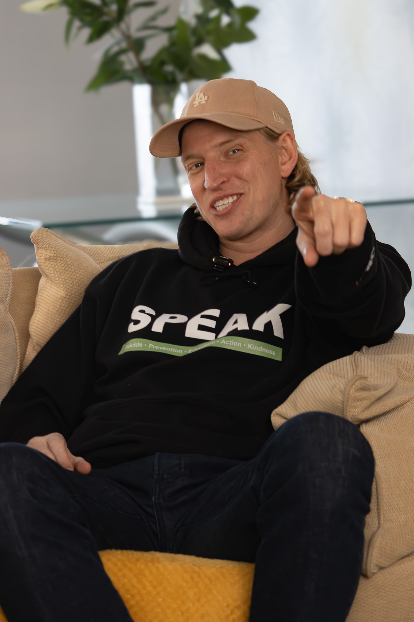 Alfie Ruffell, SPEAK's founder, smiling and pointing at the camera, wearing a SPEAK branded hoodie