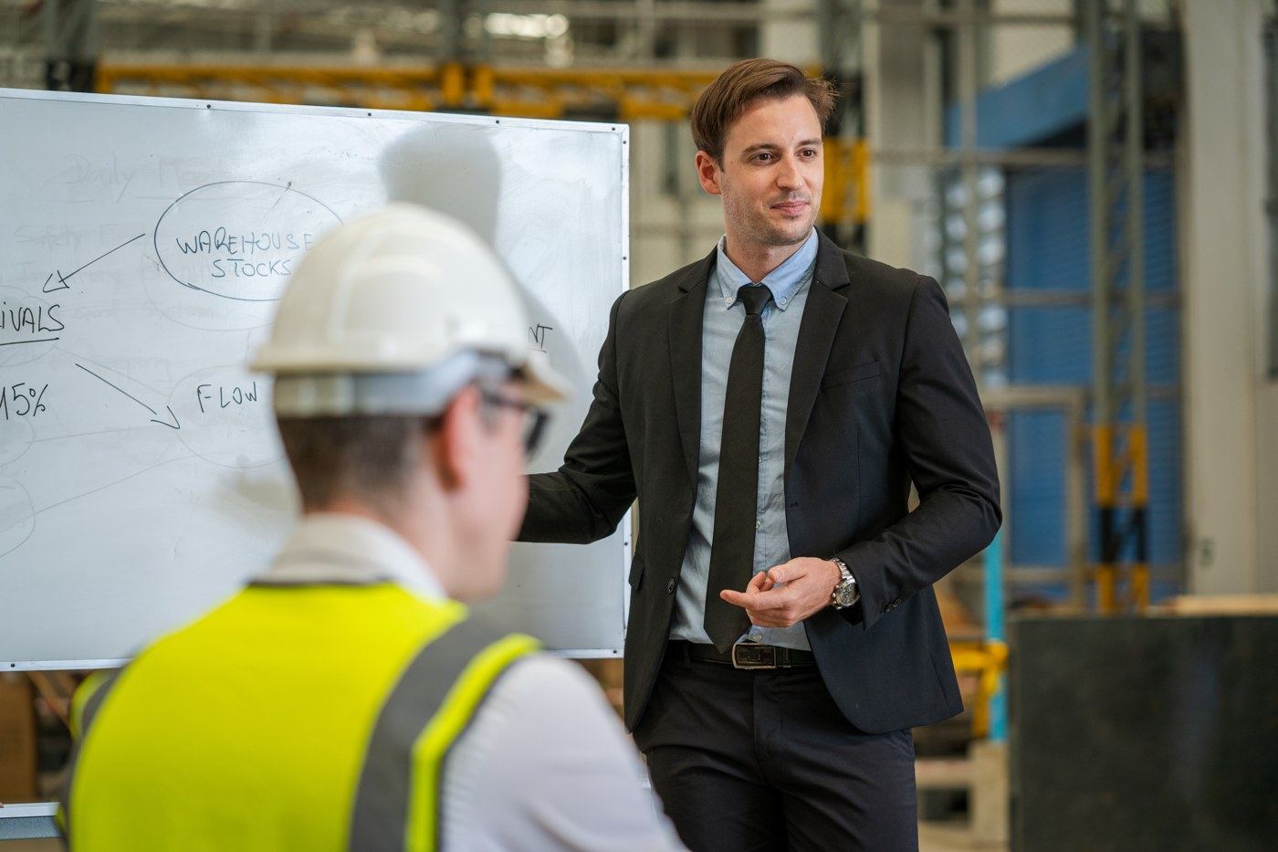 A partner in a suit presenting workforce and warehouse planning at a whiteboard to a construction team member on site.